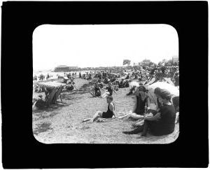 海滩的场景. 有很多人坐在伞下，在水里玩耍. 图像是黑白的
